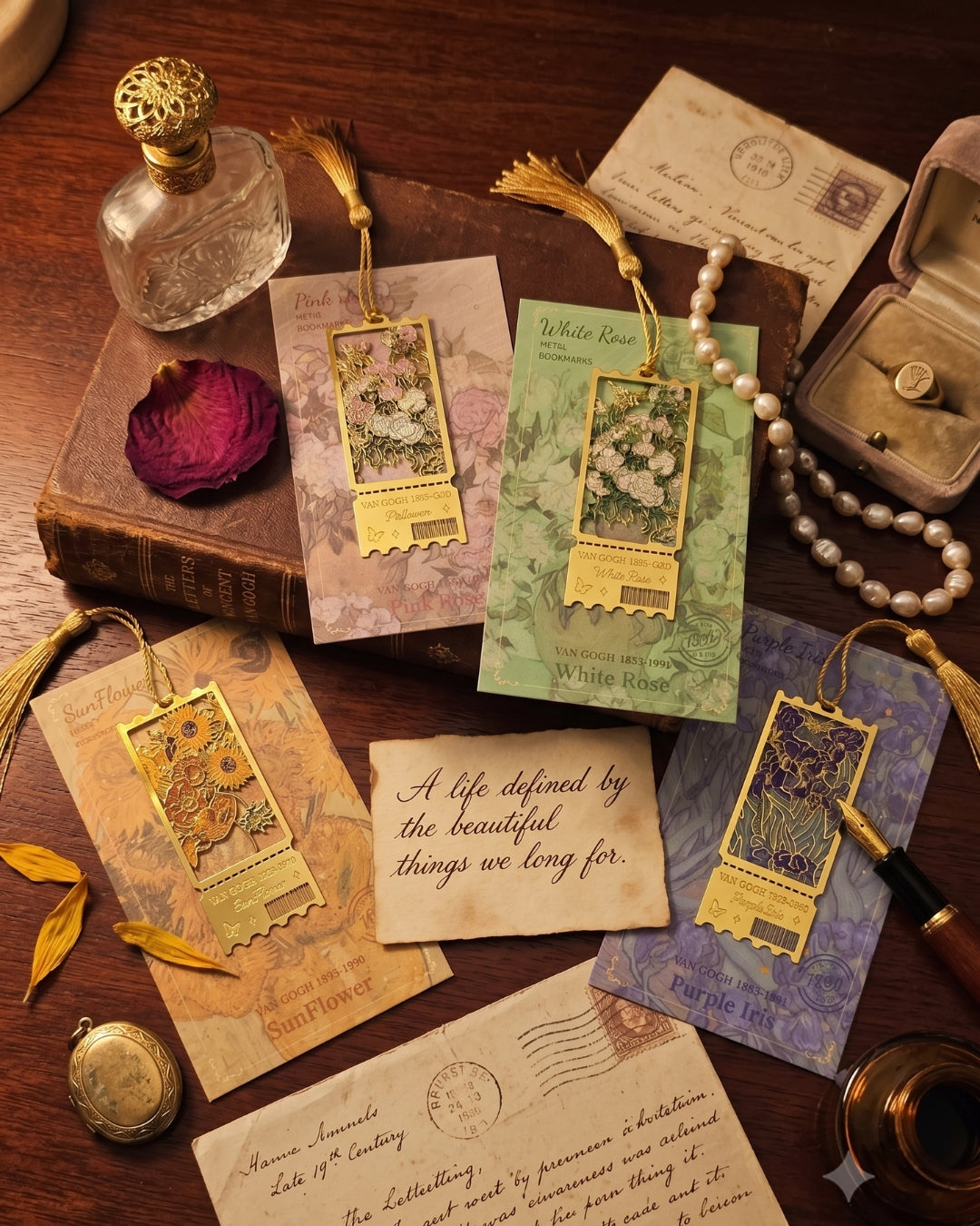A styled flat-lay of vintage-inspired bookmark cards with gold-toned metal bookmarks, arranged on a wooden tabletop with old letters, a perfume bottle, a rose petal, pearls, a ring box, and a pen.