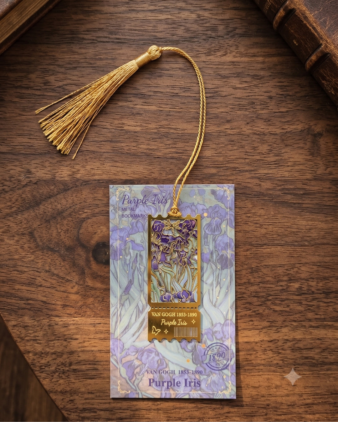 A purple iris themed bookmark or tag with a gold tassel, displayed on its illustrated backing card over a dark wooden surface.