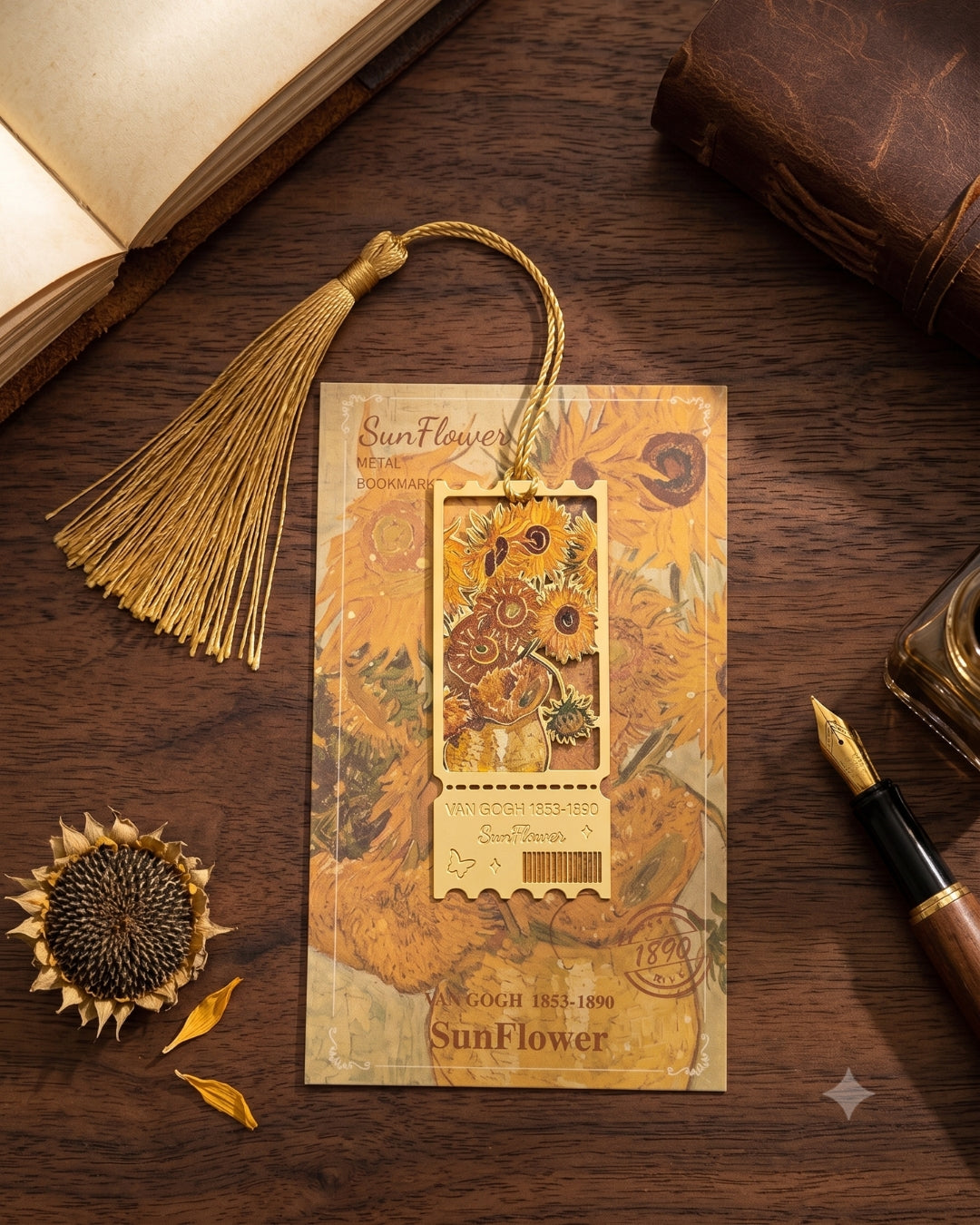 A decorative bookmark or card featuring a stylized Van Gogh-style Sunflower artwork, with a tassel loop and a small rectangular sunflower illustration. It is styled on a dark wooden surface with an open book, fountain pen, dried sunflower head, and vintage papers around it.