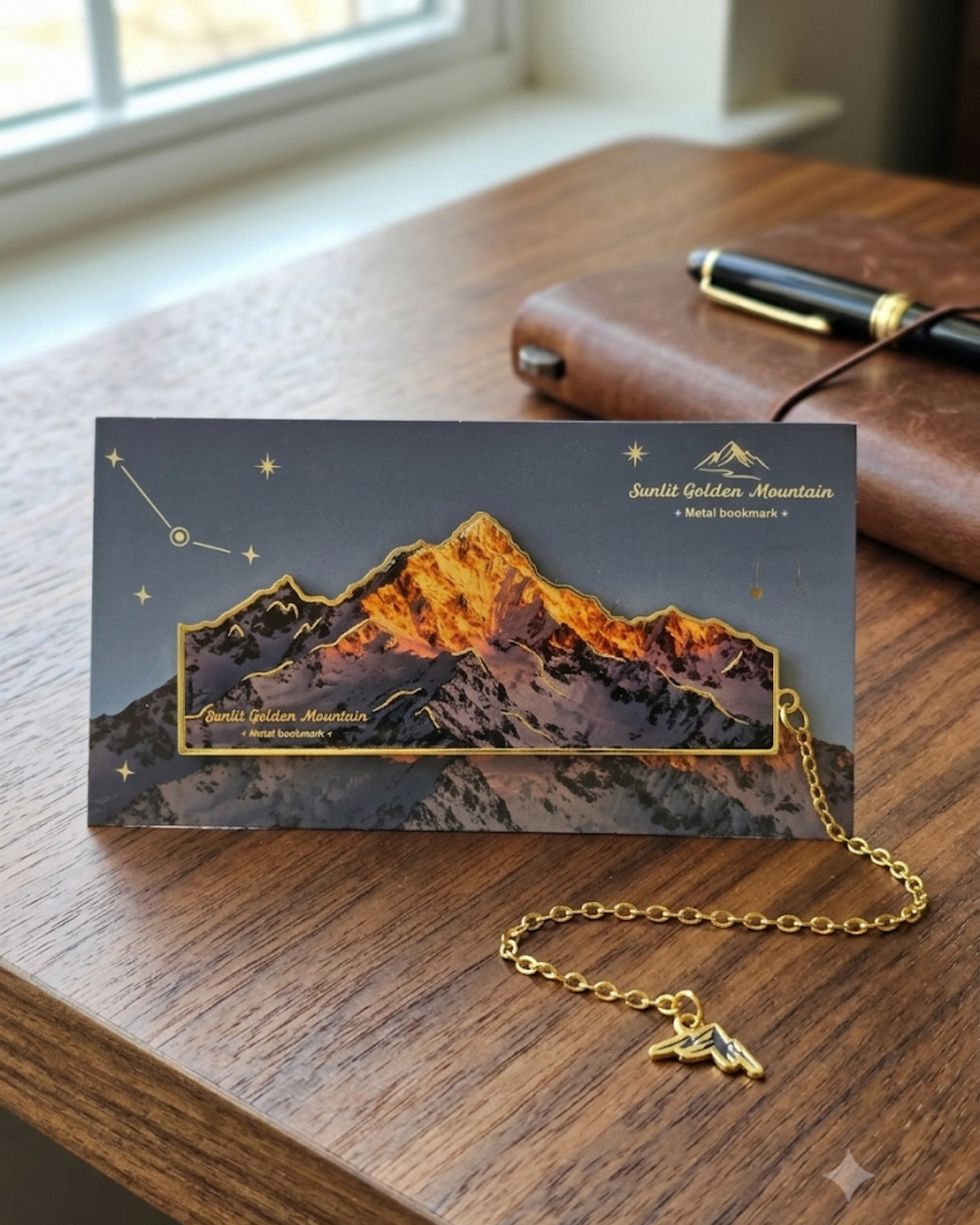 A "Sunlit Golden Mountain" metal bookmark featuring a golden mountain range against a starry night sky, attached to a delicate gold chain with a mountain charm.