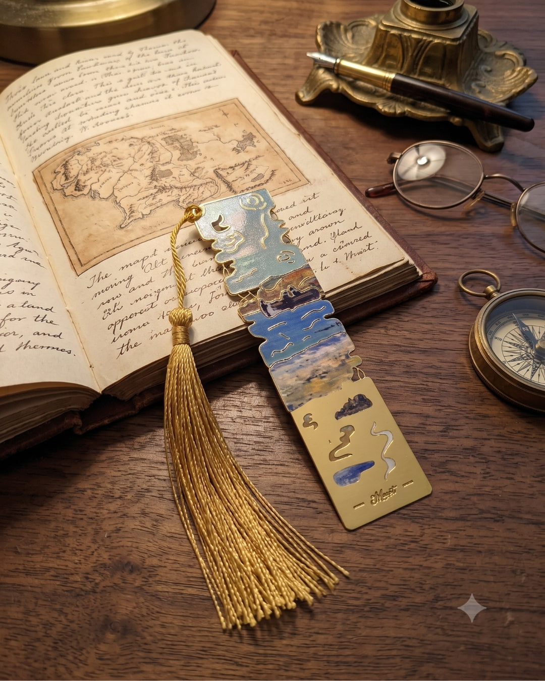 An open book with a map and handwritten text lies on a wooden surface next to a gold bookmark with a tassel, glasses, a compass, and an inkwell with a pen.