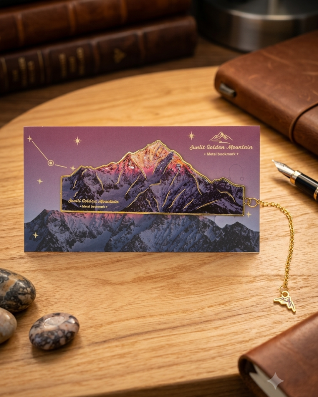 A bookmark featuring a golden mountain range illuminated by a sunset and stars, with a dangling golden charm.