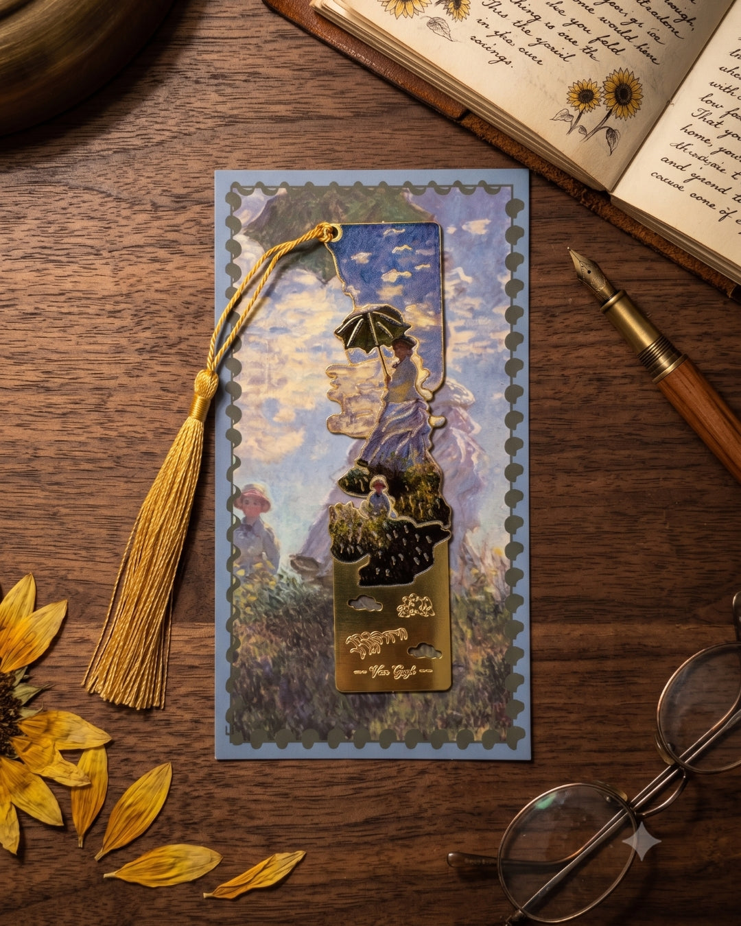 A bookmark featuring a scene from Claude Monet's painting "Woman with a Parasol - Madame Monet and Her Son" is placed on a blue postcard-like background with a gold tassel. The scene depicts a woman holding a parasol, with another figure in the background. The bookmark and postcard are on a wooden surface next to an open book with sunflowers, a fountain pen, and glasses.