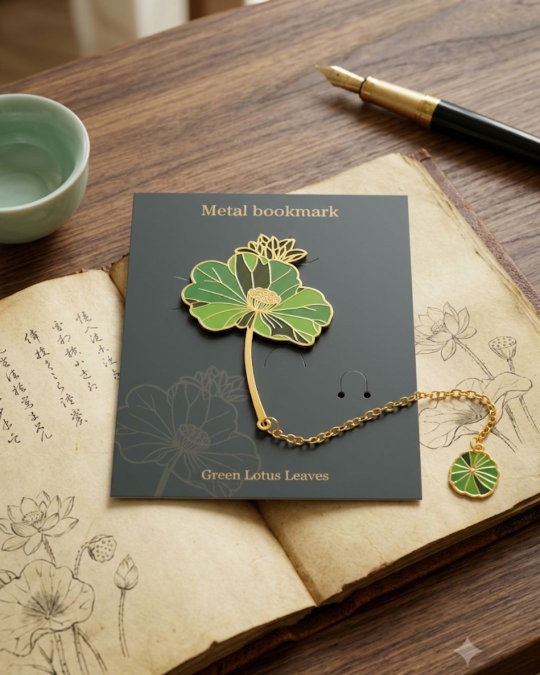 A metal bookmark shaped like a green lotus flower with a gold chain and a small green lotus charm on the end, presented on a dark gray card with "Metal bookmark" and "Green Lotus Leaves" printed on it. The bookmark rests on an open book with lotus illustrations.