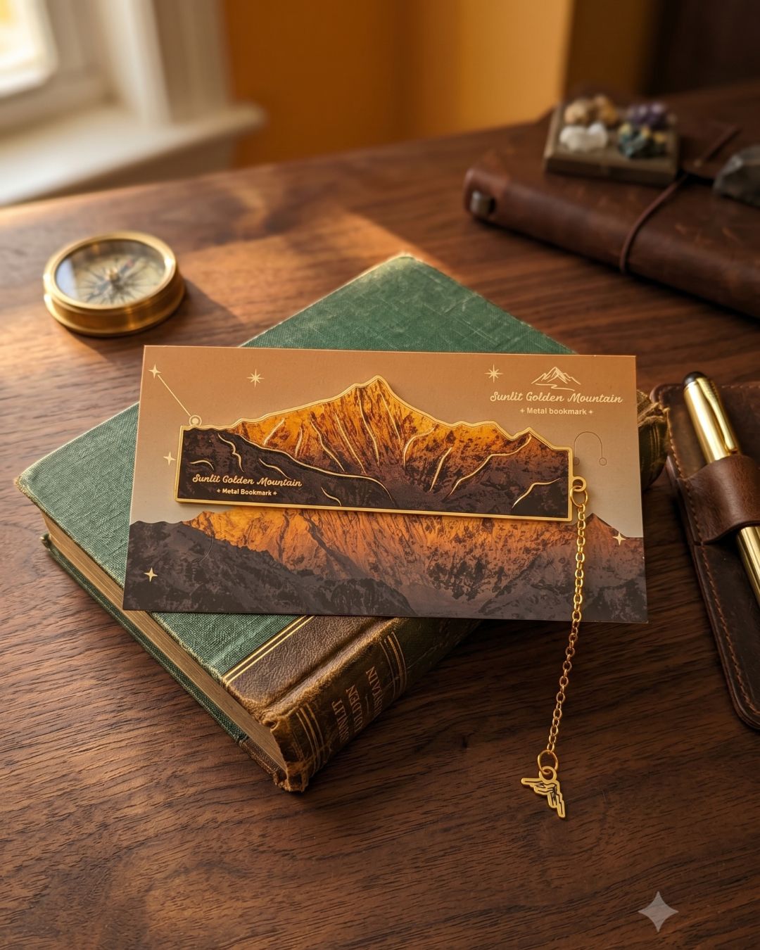 A gold metal bookmark shaped like a mountain range with the text "Smithsonian Mountains" on a card depicting a mountain landscape, resting on a vintage green book.