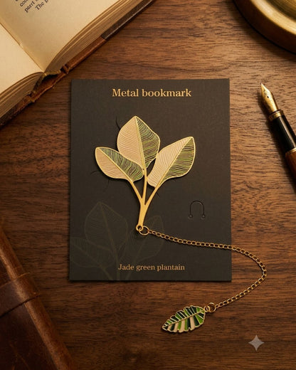 A metal bookmark shaped like a plantain leaf stem with three leaves and a decorative smaller leaf attached by a gold chain. The bookmark is displayed on a dark card with the text "Metal bookmark" and "Jade green plantain".